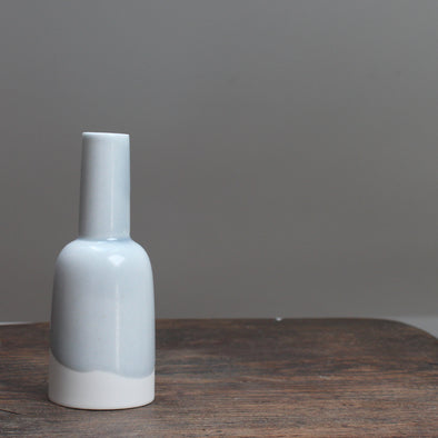 Small kiln shaped pale blue bottle with a white bottom on a wooden table 