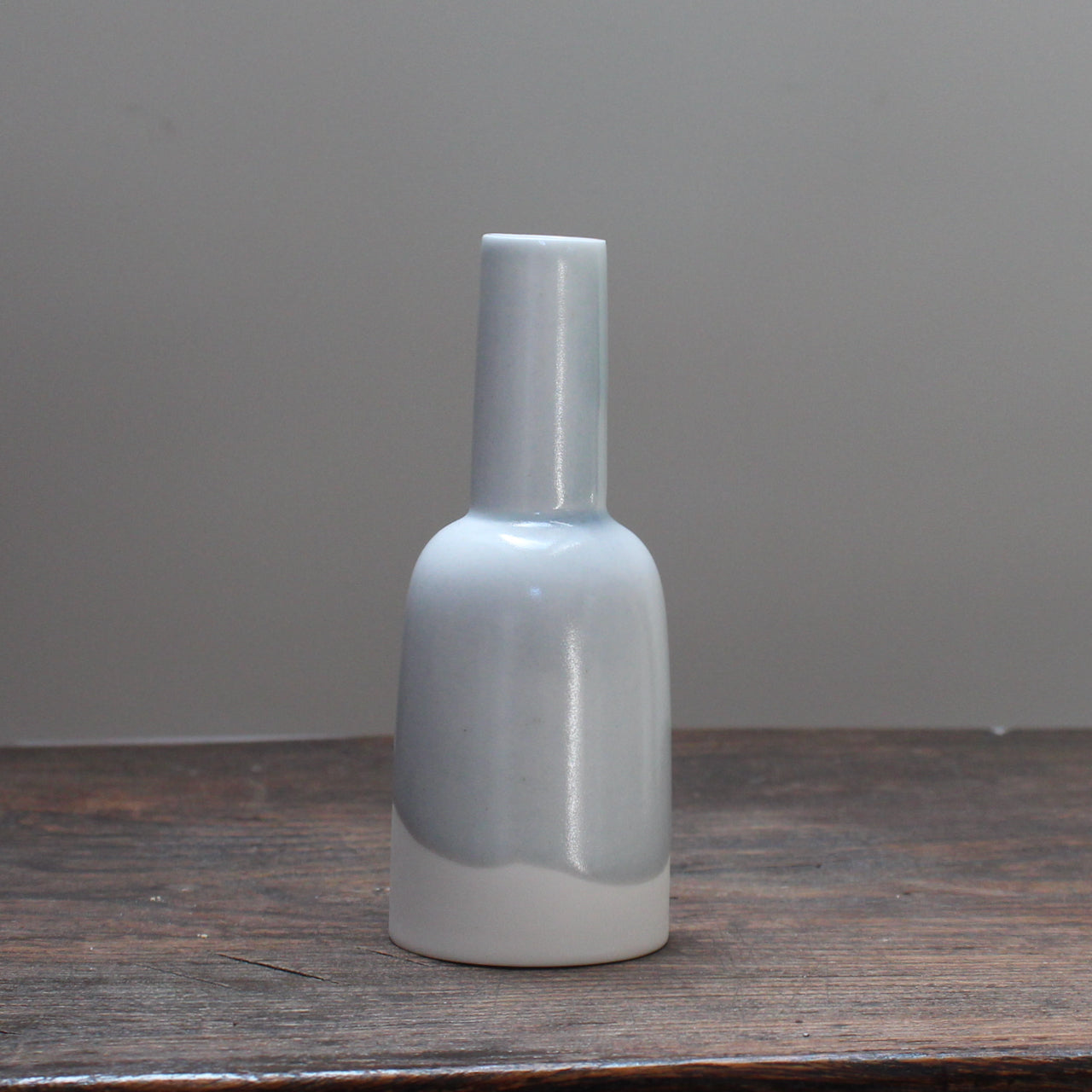 Small kiln shaped pale blue bottle with a white bottom on a wooden table