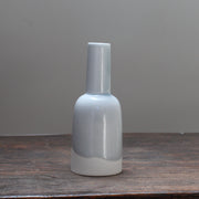 Small kiln shaped pale blue bottle with a white bottom on a wooden table 