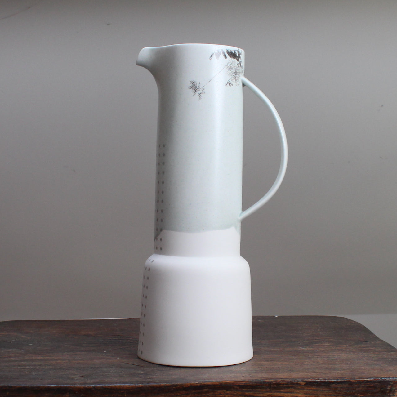 Tall pale green vase with grey pattern of flowers standing on a wooden table