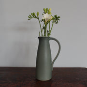 Olive green ceramic jug with handle with flowers in it by Lucy Burley on wooden table at the Byre Gallery 