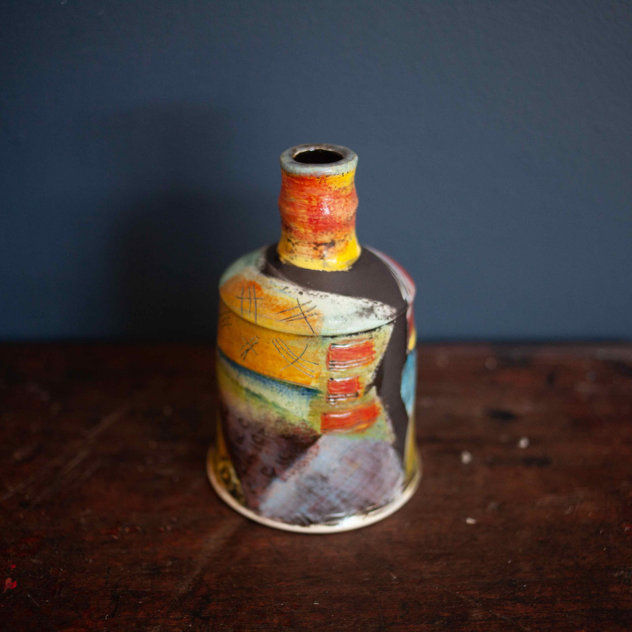 A brightly coloured pottery bottle by John Pollex on a wooden table