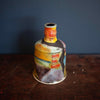 A brightly coloured pottery bottle by John Pollex on a wooden table 