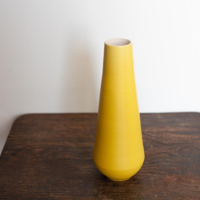 tall yellow vase by Lucy Burley on a wooden table
