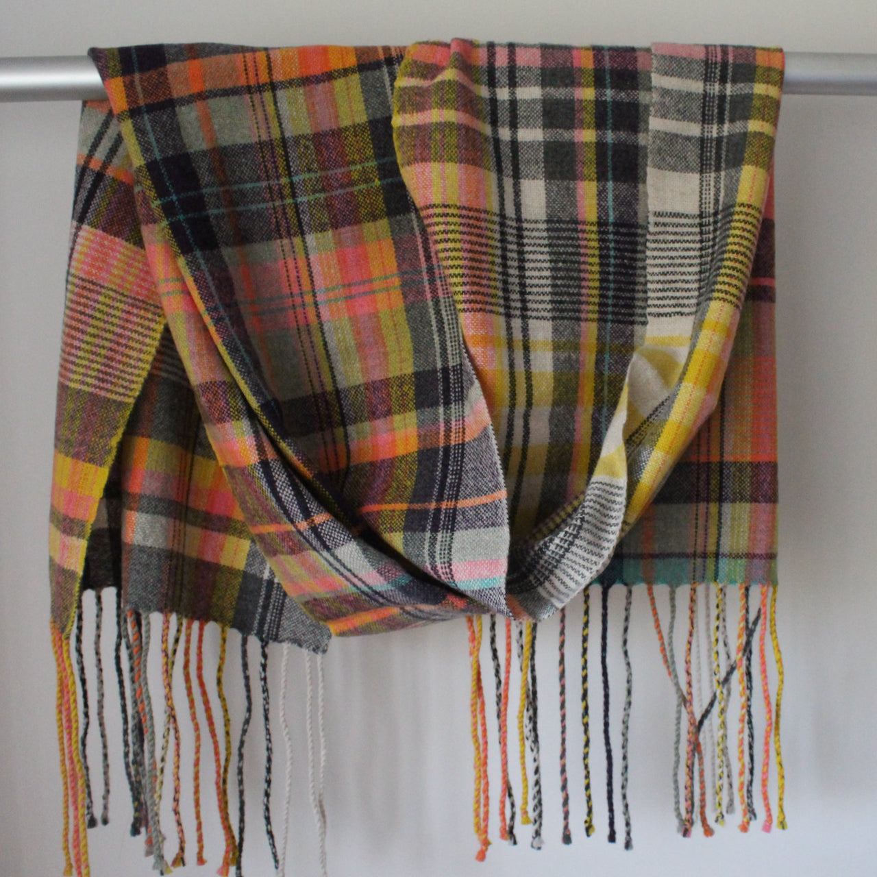 A handwoven scarf with orange, yellow  colours  hanging over a rail