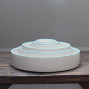Six stacked white round bowls with a blue rim