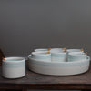 Seven small bowls with turquoise stripes on the outside and wooden spoons set inside a larger serving dish