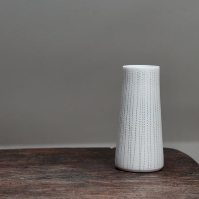 narrow ceramic white stem vase with vertical blue lines on a wooden table  