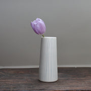 narrow ceramic white stem vase with vertical blue lines with a purple tulip in it
