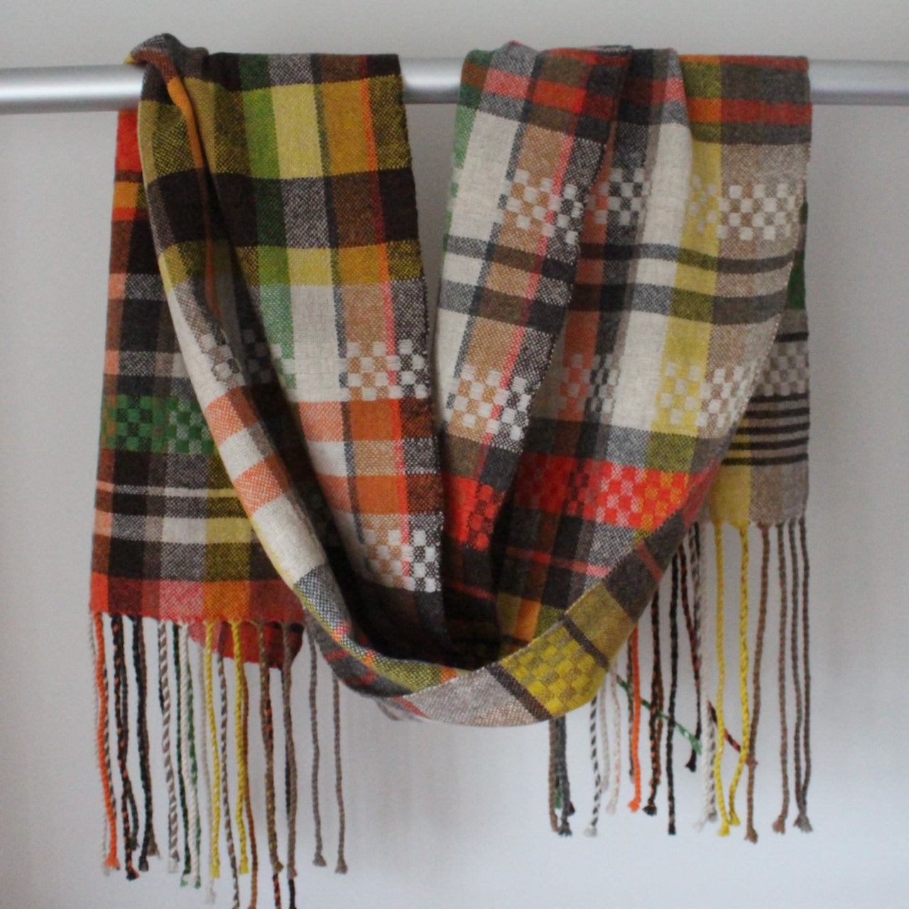 Close up of handwoven scarf in shades of yellow, green and red hanging over a display rail