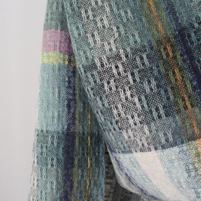 a handwoven scarf by UK textile artist Teresa Dunne it's in shades of green, blue, orange and pink.