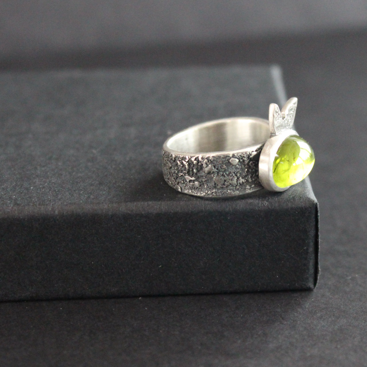 Carin Lindberg - Peridot ring in textured sterling silver with textured leaf on a raised display box.