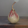 A cream and pink ceramic pear with glaze details and a gold stalk by ceramicist Remon Jephcott.