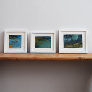 three small abstract landscape paintings by Alice Robinson-Carter in dark blues and yellows they are mounted and framed in white 