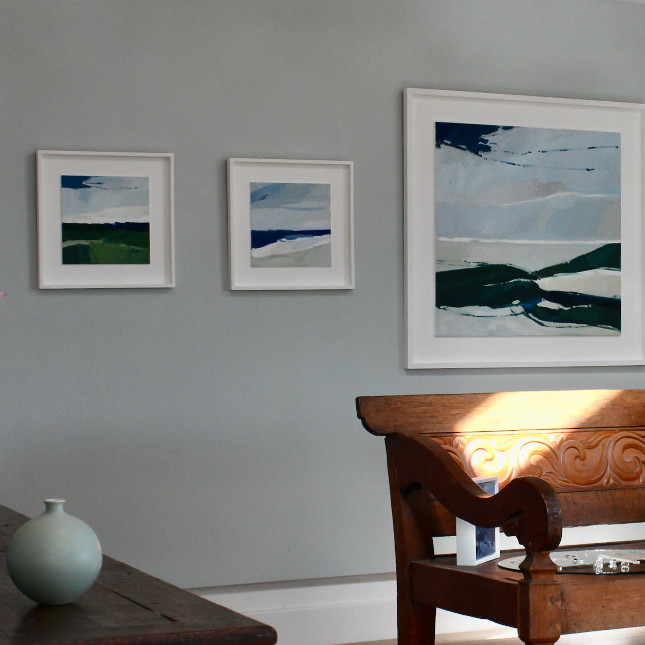 Three abstract landscape paintings in pale blues and greens hanging on a gallery wall
