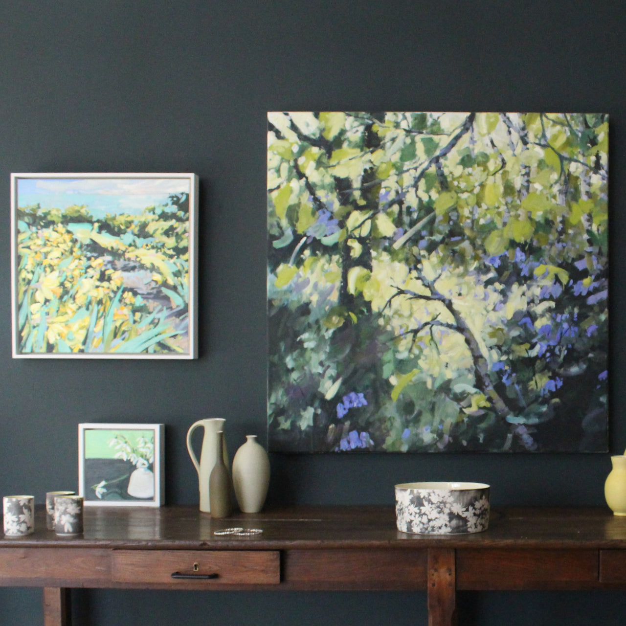 Jill Hudson landscape paintings on a dark wall above a collection of ceramics 