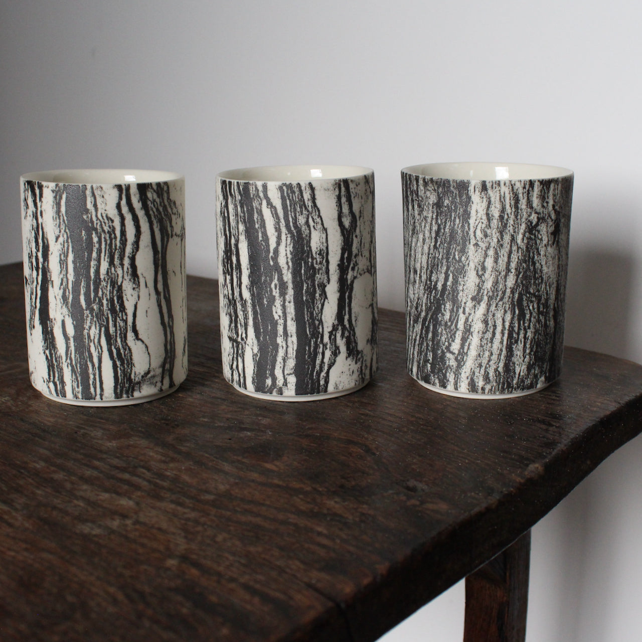 trio of small ceramic beakers by UK ceramicist Heidi Harrington with a black and white photo image of tree bark on the the exterior and cream glazed interior