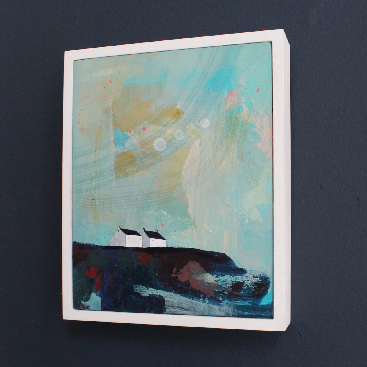 framed coastal painting by Emma Carlisle of two white houses on a cliff with a turquoise sky