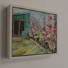 a framed Jill Hudson oil painting of pink flowers in a garden border with a deck chair and the edge of a green shed 