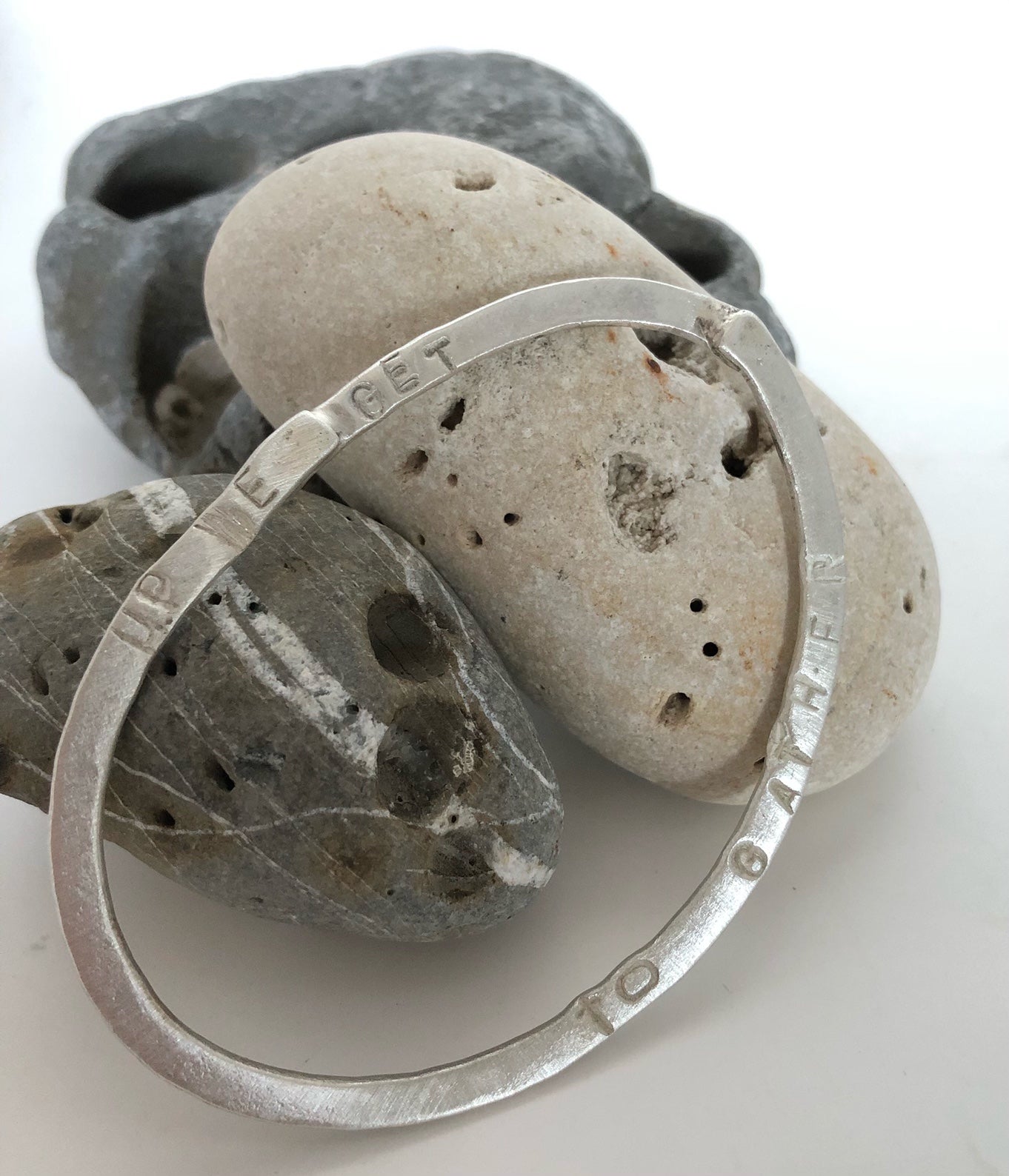 silver bangle with the words up we get to gather embossed on it by jeweller Lizzie Weir of Anatole Design photographed on some stones