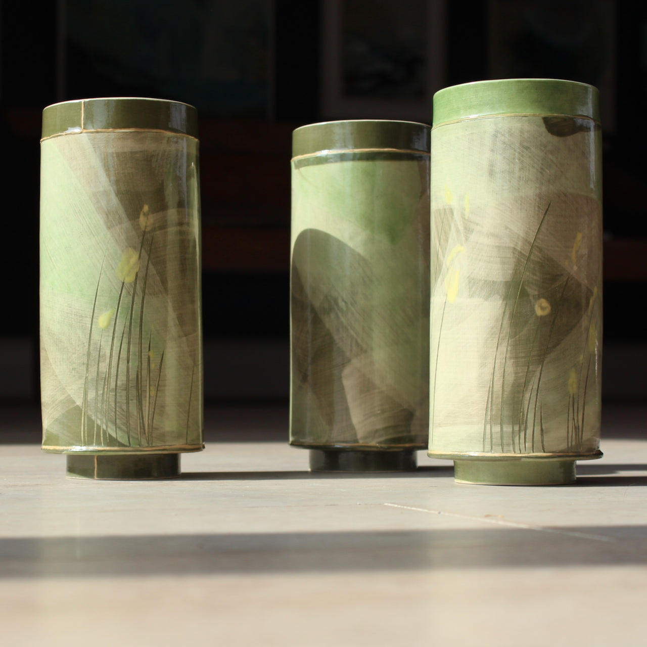 a trio of tall cylindrical ceramic vessels in green glaze decorated with yellow flowers made by UK ceramicist Emily-Kriste Wilcox.