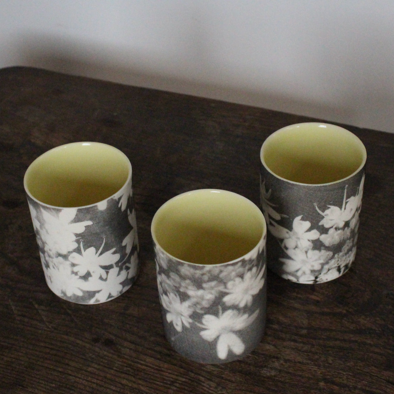 a trio of small ceramic beakers by UK ceramicist Heidi Harrington with a black and white photo image of flower petals on the the exterior and pale yellow glazed interior.