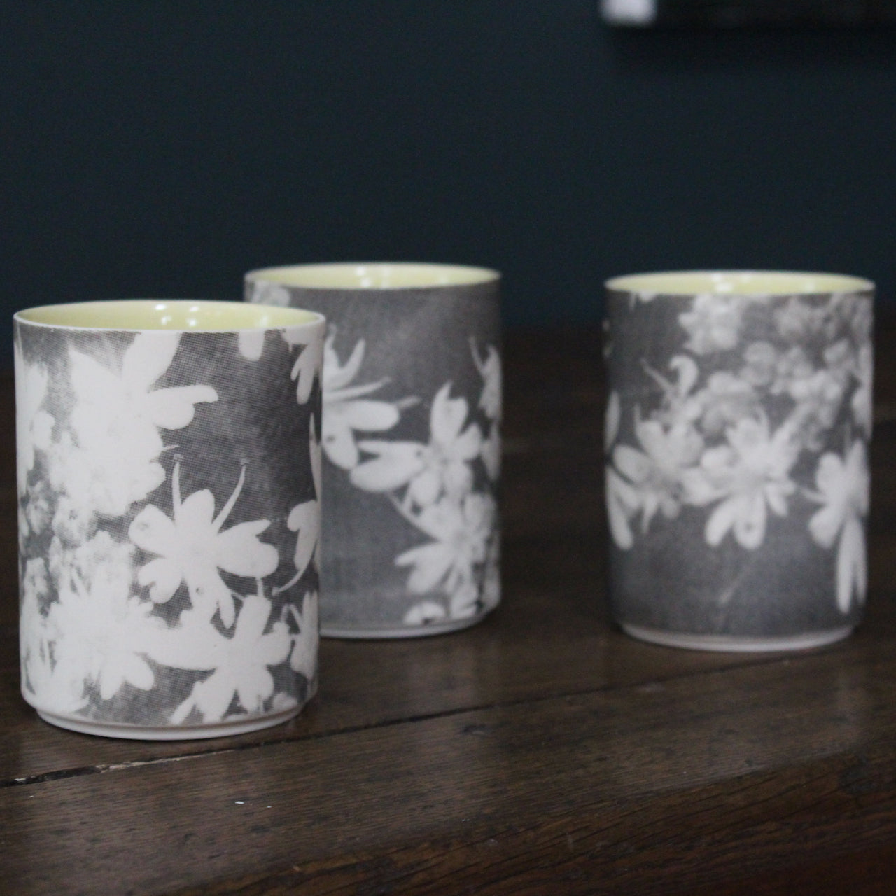 trio of small ceramic beakers by UK ceramicist Heidi Harrington with a black and white photo image of flower petals on the the exterior and pale yellow glazed interior